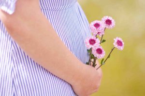 живот беременной женщины с цветами в руках