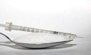 шприц с инсулином лежит на ложке, в которой сахарный песок