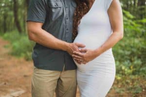 беременная девушка с мужем держат руками ее живот