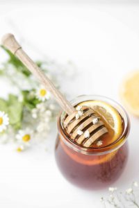 Мед в стеклянной таре с деревянной ложкой и ломтиком лимона внутри