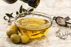 оливковое масло наливается из бутылки в стеклянную пиалу, а сбоку на столе лежат оливки