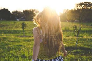 девушка с длинными светлыми волосами гуляет по саду навстречу солнцу