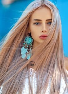 девушка с длинными светлыми волосами и голубой серьгой в виде ловца снов