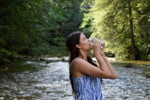 девушка пьет воду из стеклянного стакана на фоне реки