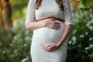 беременная девушка в белом платье держит руками живот