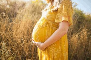 беременная девушка в желтом платье на фоне поля