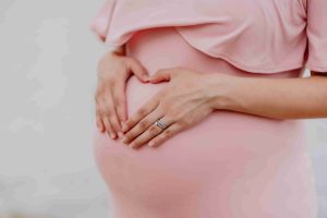 беременная девушка в розовом платье держит живот руками