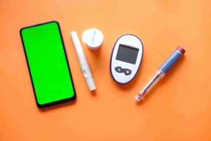 глюкометр, таблетки от диабета и телефон на оранжевой поверхности