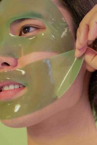 девушка наносит зеленую тканевую маску на лицо