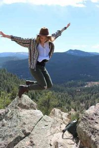 девушка в шляпе прыгает на камнях на фоне гор