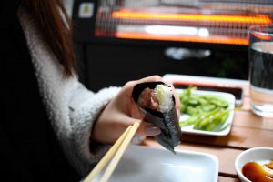суши ролл в руках у девушки, которая сидит за столом в кафе