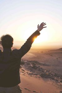 мужчина поднимает руки кверху на фоне гор и восхода солнца