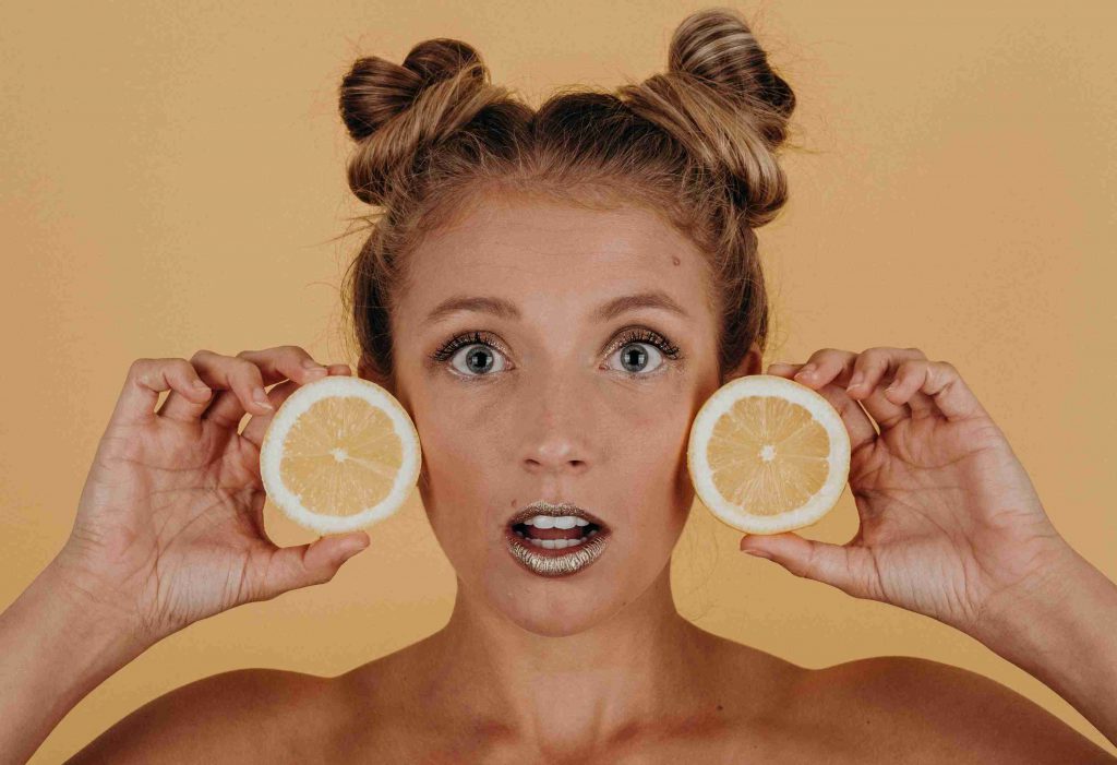 девушка держит половинки лимонов возле лица