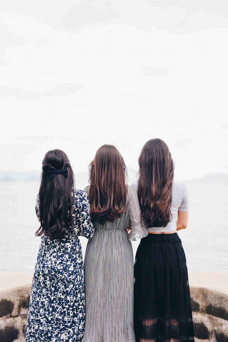 три девушки с длинными волосами и в платьях стоят спиной