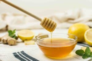лимон и мед стоят на столе, пчелиный продукт набирается из стеклянной пиалы деревянной ложкой