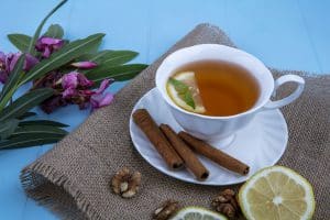 Черный чай с лимоном в белой фарфоровой чашке с ломтиком цитруса и корицей, грецкими орехами и цветами по бокам