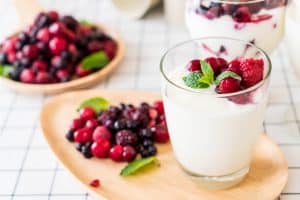 йогурт в стакане с ягодами на деревянной тарелке