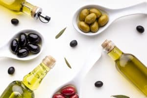зеленые, черные и красные оливки на белых ложках и бутылки с оливковым маслом